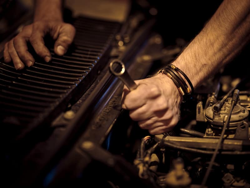 Manos con grasa reparando el motor de un coche con una llave inglesa